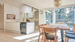 A modern kitchen with white cabinetry, a built-in oven, and a dining area with a wooden table and chairs. - 8 Person Holiday Home in Nexo (Nexø)