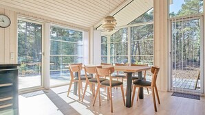 A dining area with a wooden table and chairs, large windows, and a view of the forest. - 8 Person Holiday Home in Nexo (Nexø)