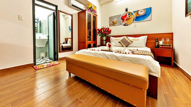 A modern hotel room with a wooden floor, a large bed with white bedding, a bench, a bedside table with a bottle and glasses, and a mirror. - HANZ Cao Gia Hai Hotel (Ho Chi Minh City)