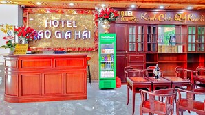 A hotel reception area with a red wooden counter, a green vending machine, and a seating area with wooden tables and chairs. - HANZ Cao Gia Hai Hotel (Ho Chi Minh City)