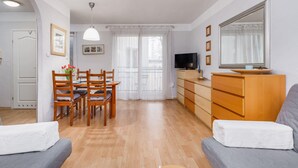 Una sala de estar con un sofá, una mesa de comedor con sillas, un televisor, un aparador y un espejo grande.