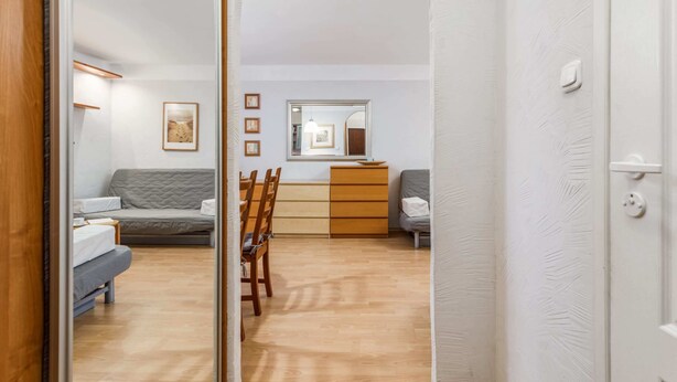 Un interior moderno con suelo de madera, un sofá gris, una mesa de comedor de madera y una pared blanca con cuadros enmarcados.