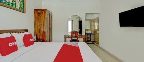 A hotel room with a bed, a TV, a wooden wardrobe, a desk, and a bathroom visible through an archway.