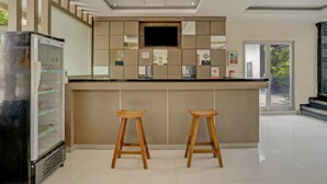 A modern kitchen with a central island, two wooden stools, a refrigerator, and a flat-screen TV mounted above the island. - Kiki Residence Bali (Denpasar)