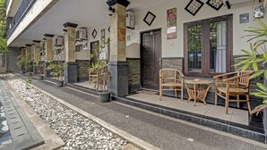A covered outdoor seating area with stone pillars, potted plants, and wooden furniture. - Kiki Residence Bali (Denpasar)