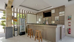 A modern kitchen area with a bar counter, two wooden stools, a refrigerator, a microwave, and a television mounted on the wall. - Kiki Residence Bali (Denpasar)