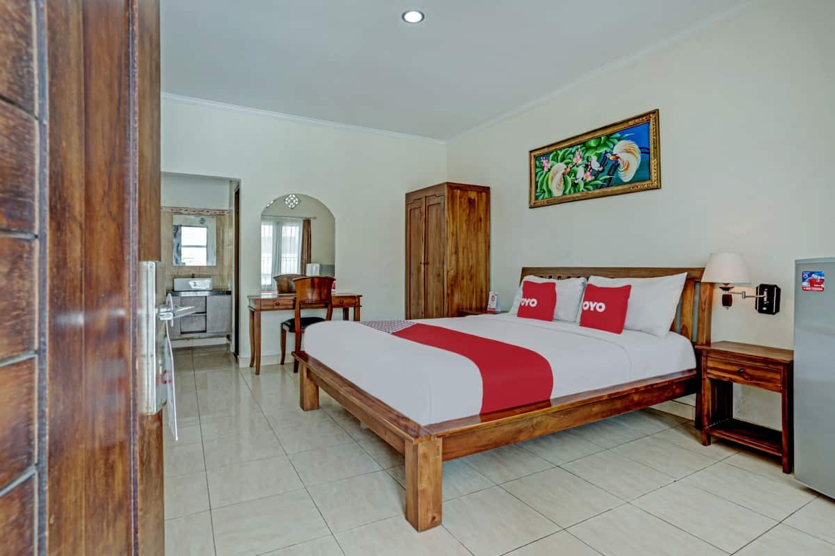 A hotel room with a wooden bed, a desk with a chair, a wardrobe, and a painting on the wall.