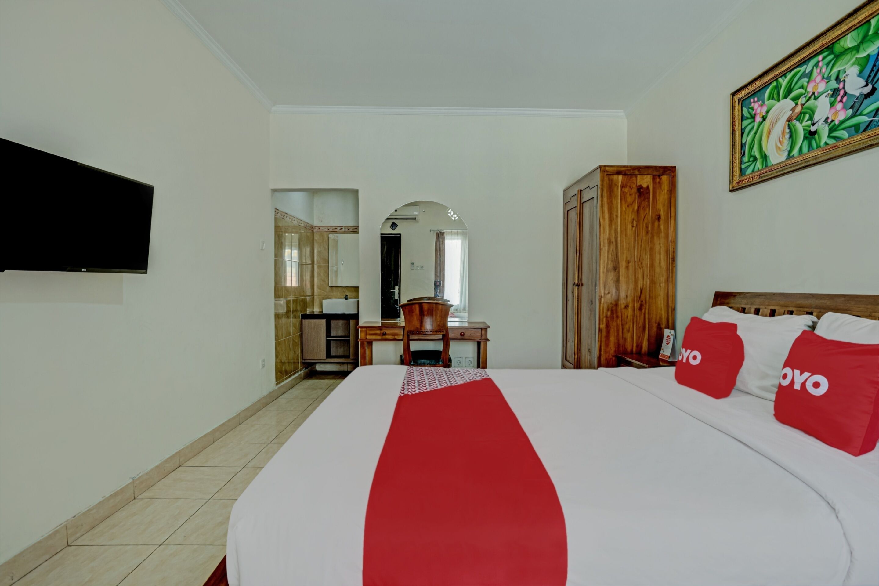 Habitación de hotel con una cama grande, un televisor montado en la pared, un armario de madera y un cuadro.