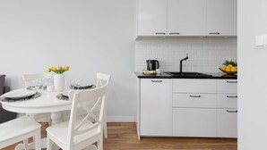 Une cuisine moderne avec des meubles blancs, un plan de travail noir et un coin repas comprenant une table blanche dressée pour quatre personnes.