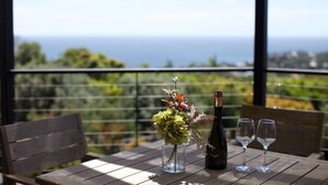 Una mesa con una botella y vasos, un florero con flores y vista al mar.