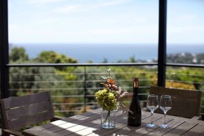 A table with a bottle and glasses, a vase with flowers, and a view of the sea.