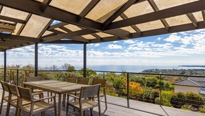 Una terraza al aire libre con una mesa y sillas de madera, con vistas a un paisaje marino.