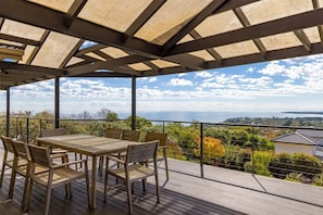 An outdoor deck with a wooden table and chairs, overlooking a scenic view of the sea and landscape.
