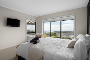 A bedroom with a large bed, a flat-screen TV, and a balcony with a view.