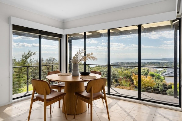 A dining area with a round table and chairs, large windows with a view of the landscape.