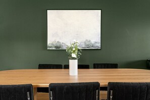A conference room with a wooden table, black chairs, a white vase with flowers, and a framed painting on the wall.