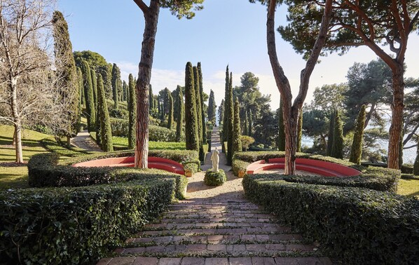 A formal garden with a central statue, trimmed hedges, and a paved pathway.