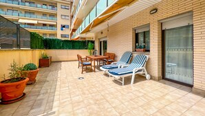 A covered outdoor patio with a table and chairs, potted plants, and a view of a multi-story building. - Apt, 4 pax LLoret de Mar - Fenals - wifi, community pool a few meters from the beach. Vivalidays Elia. (Lloret de Mar)