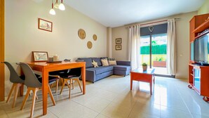 A modern living room with a dining area, a sofa, a TV, and a large window with curtains. - Apt, 4 pax LLoret de Mar - Fenals - wifi, community pool a few meters from the beach. Vivalidays Elia. (Lloret de Mar)