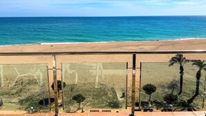 A beach view from a balcony with a clear sky, sandy beach, and some vegetation. - Apartment 4/5 Pax with direct access to the beach. It has a community pool. Excellent location, bars, restaurants, shops and promenade. Free WIFI. Vivalidays Mar. (Santa Susana)