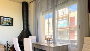A room with a fireplace, a dining table with chairs, a window with curtains, and a painting on the wall. - Apartment 4/5 Pax with direct access to the beach. It has a community pool. Excellent location, bars, restaurants, shops and promenade. Free WIFI. Vivalidays Mar. (Santa Susana)