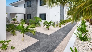A modern two-story house with a stone facade, a paved driveway, and a variety of tropical plants. - Penthouse Mesa Bonita – Modern Caribbean Luxury (Jan Thiel)