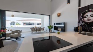 A modern kitchen with a large island, a dining area with a table and chairs, and a view of a building outside. - Penthouse Mesa Bonita – Modern Caribbean Luxury (Jan Thiel)