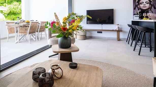 A modern living room with a large TV, a dining area with wicker chairs, and a wooden coffee table with decorative items. - Penthouse Mesa Bonita – Modern Caribbean Luxury (Jan Thiel)