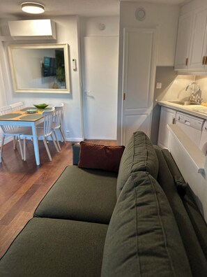 Ein modernes Wohnzimmer mit einem grünen Sofa, einem Esstisch mit Stühlen und einer Küchenzeile inklusive Spüle und Schränken.