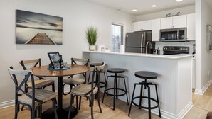 Une cuisine moderne avec des meubles blancs, un îlot central doté de tabourets et une table à manger avec des chaises.