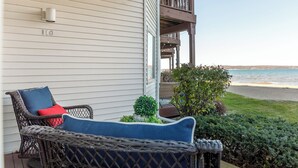 Une chaise en osier avec des coussins, une petite plante en pot et un balcon donnant sur une plage.