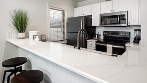 Une cuisine moderne avec des meubles blancs, un réfrigérateur noir, un four à micro-ondes en acier inoxydable et une cuisinière noire.