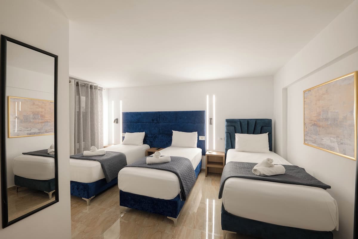 Habitación de hotel con tres camas, un espejo grande y obras de arte en las paredes.