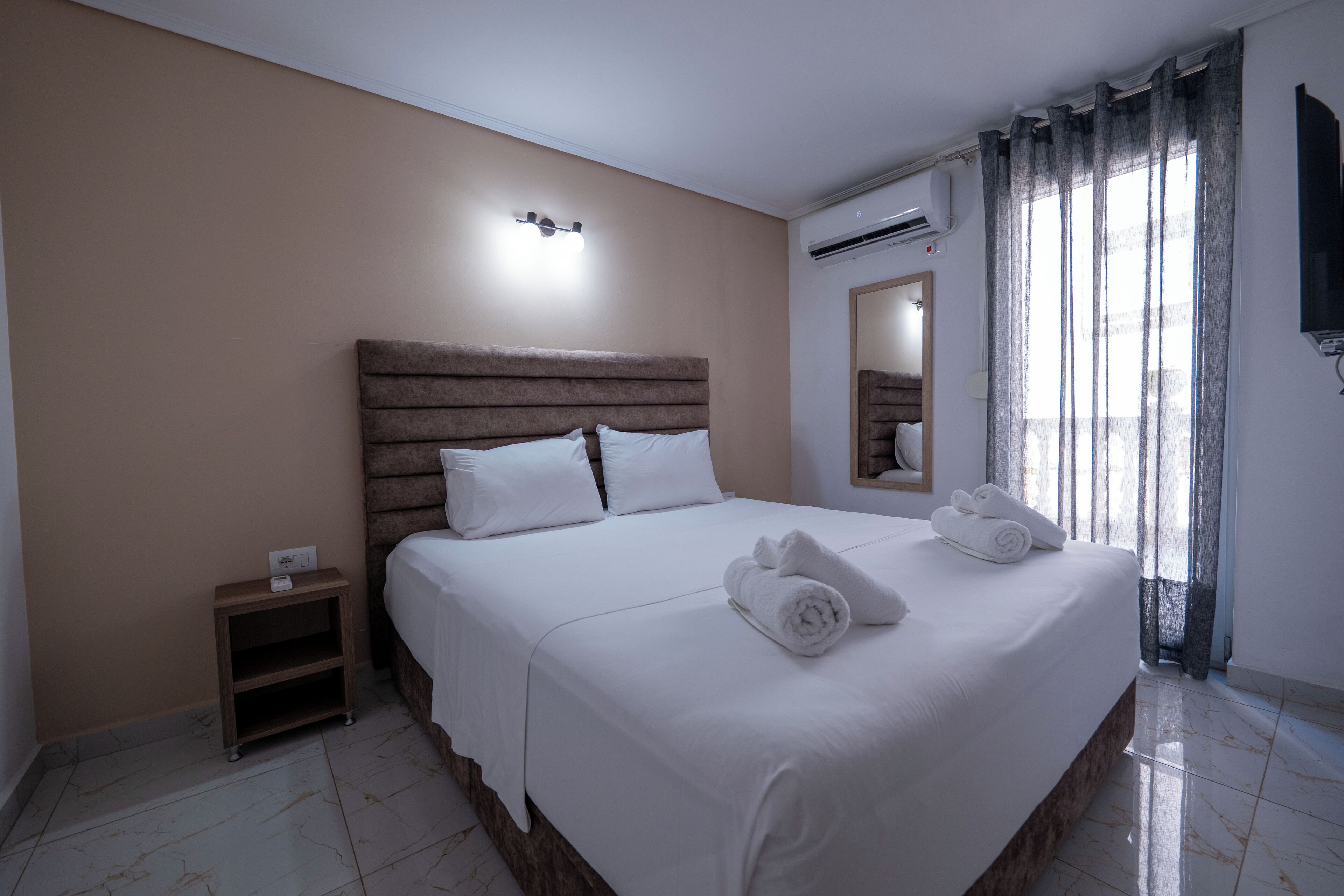 Een hotelkamer met een groot bed, een nachtkastje, een spiegel en een airconditioner.