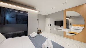 A modern hotel room with a large bed, a TV, a mirror, and a bathroom vanity. - Elite Hotel (Sarandë)