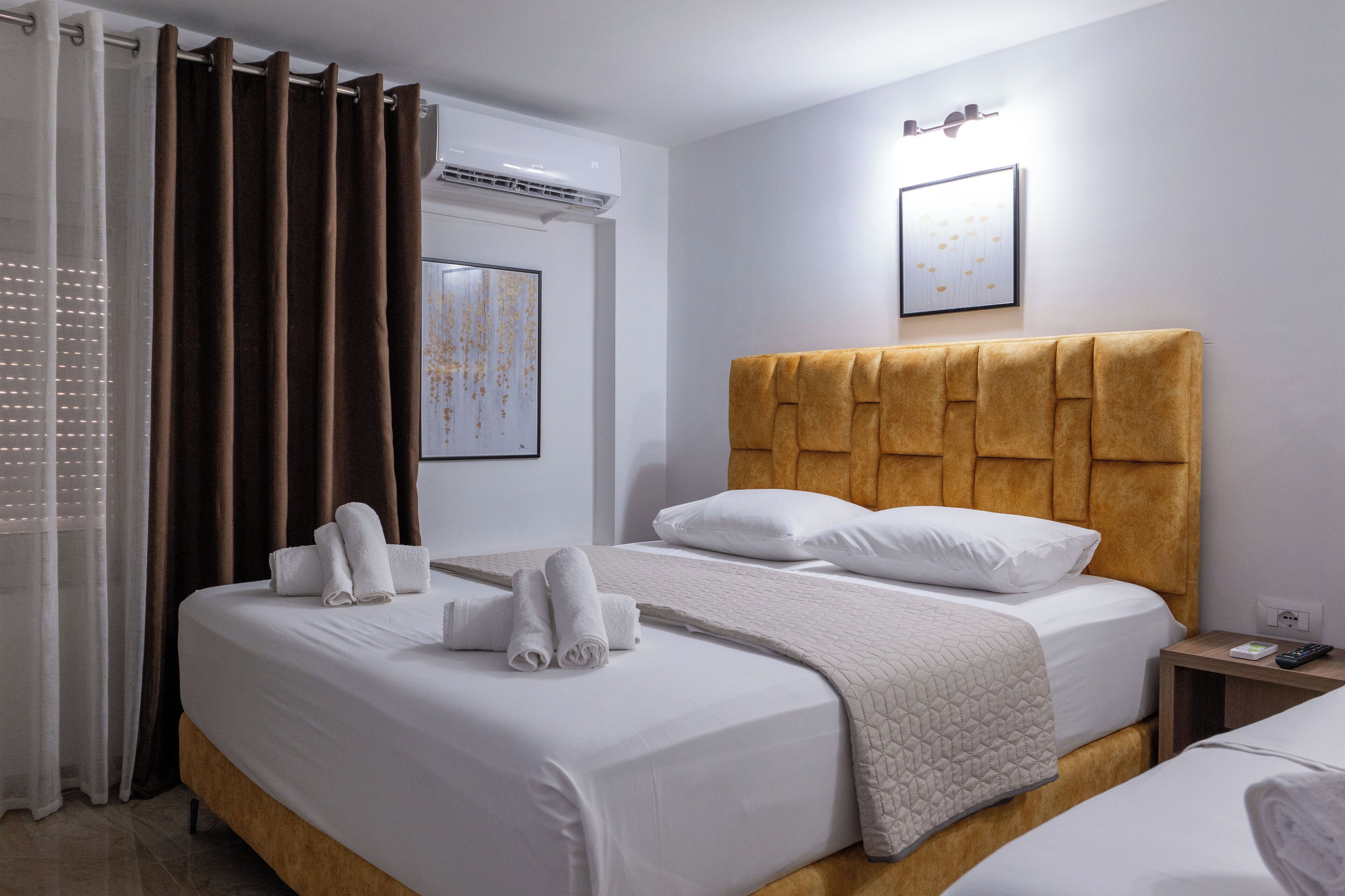 A hotel room with a large bed, a bedside table with a remote control, and a wall-mounted air conditioner.