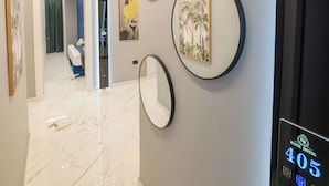 A modern hotel hallway with a marble floor, circular wall mirrors, and a digital display showing room number 405. - Elite Hotel (Sarandë)