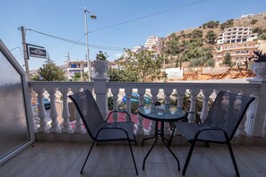 Un balcon avec deux chaises et une table, donnant sur une colline parsemée de bâtiments.