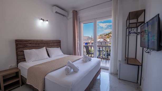 A hotel room with a bed, a TV, a balcony, and a view of buildings. - Elite Hotel (Sarandë)