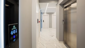 A modern hotel hallway with a digital display indicating room number 401, a marble floor, and a sleek elevator. - Elite Hotel (Sarandë)