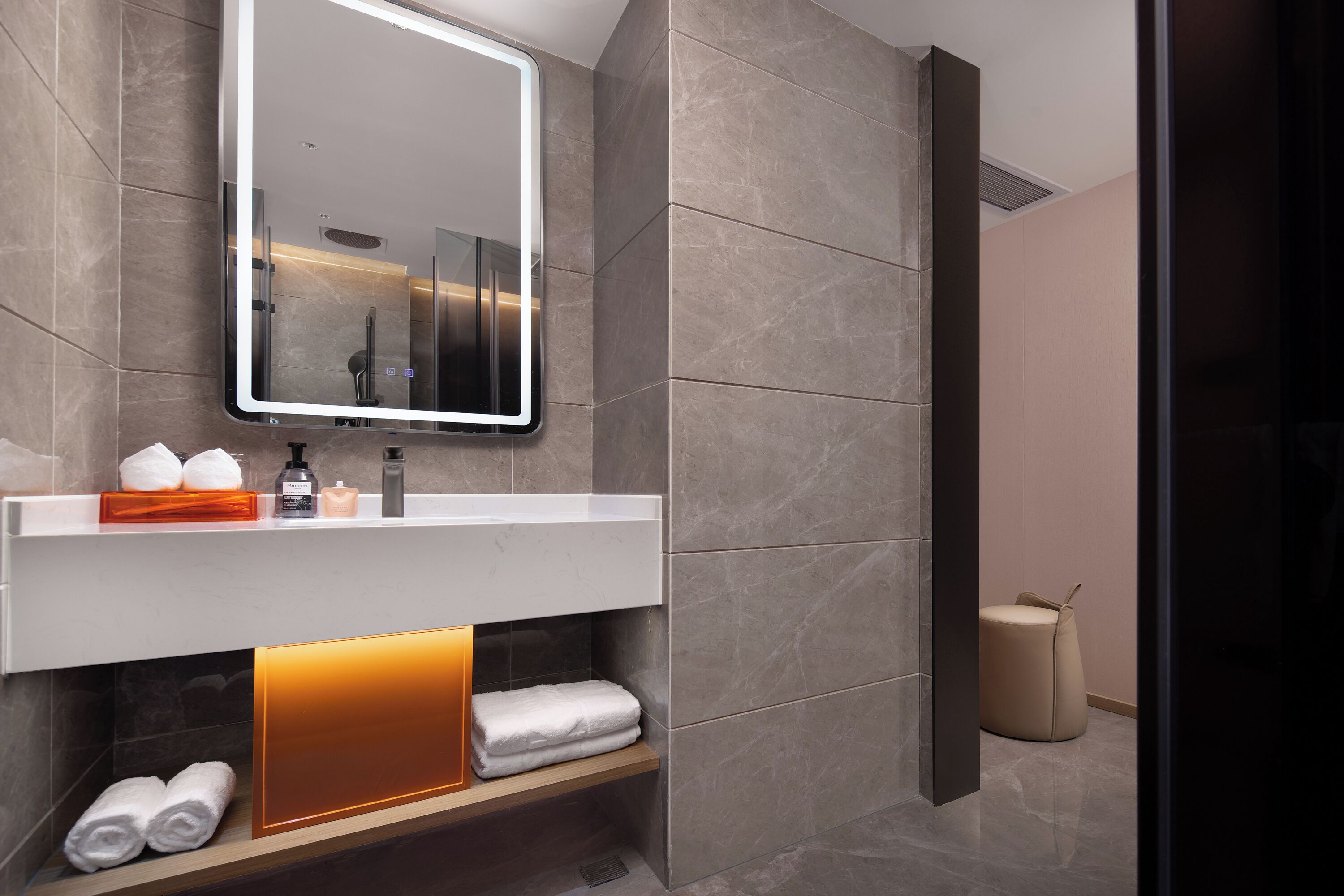 A modern bathroom with a large mirror, a towel rack, and a shelf with toiletries.