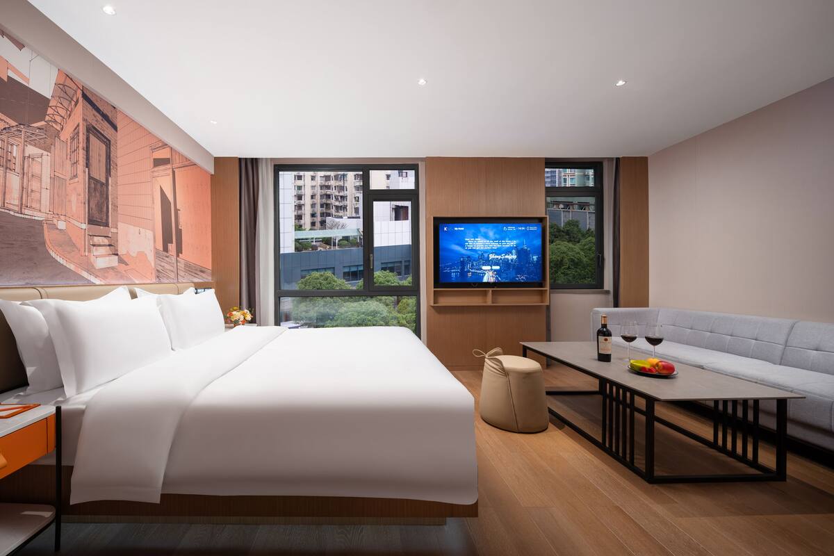 Una habitación de hotel moderna con una cama grande, televisión, sofá y mesa de comedor.