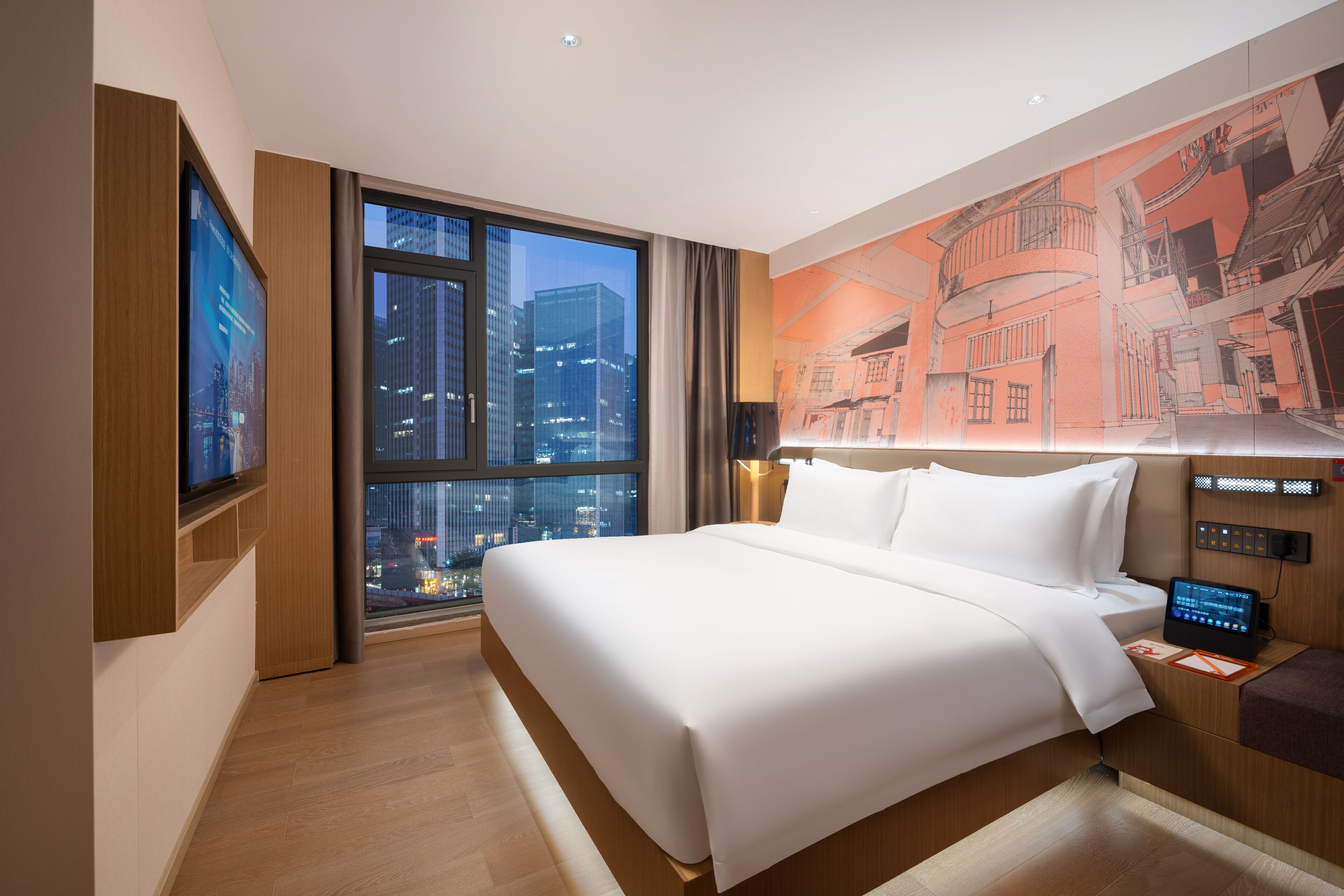 Un hotel moderno con una cama grande, vistas a la ciudad, un panel de control digital y un televisor montado en la pared.