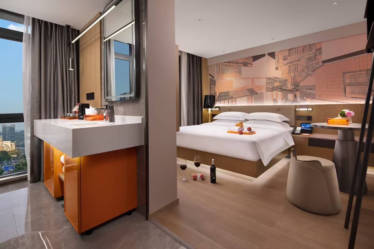 Habitación de hotel moderna con una cama grande, baño con tocador y vista a la ciudad.