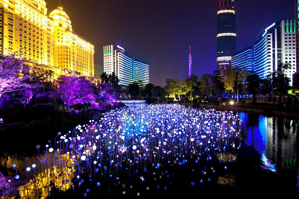 Un paisaje urbano nocturno con edificios iluminados y una fuente con luces flotantes.