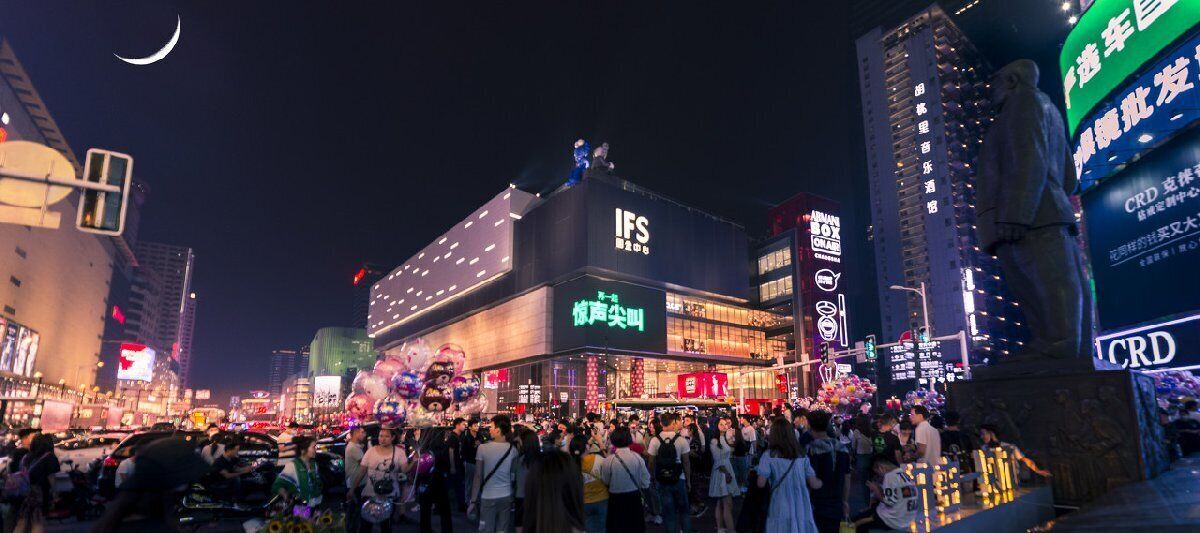 Una bulliciosa calle urbana nocturna con edificios iluminados y una multitud de gente.