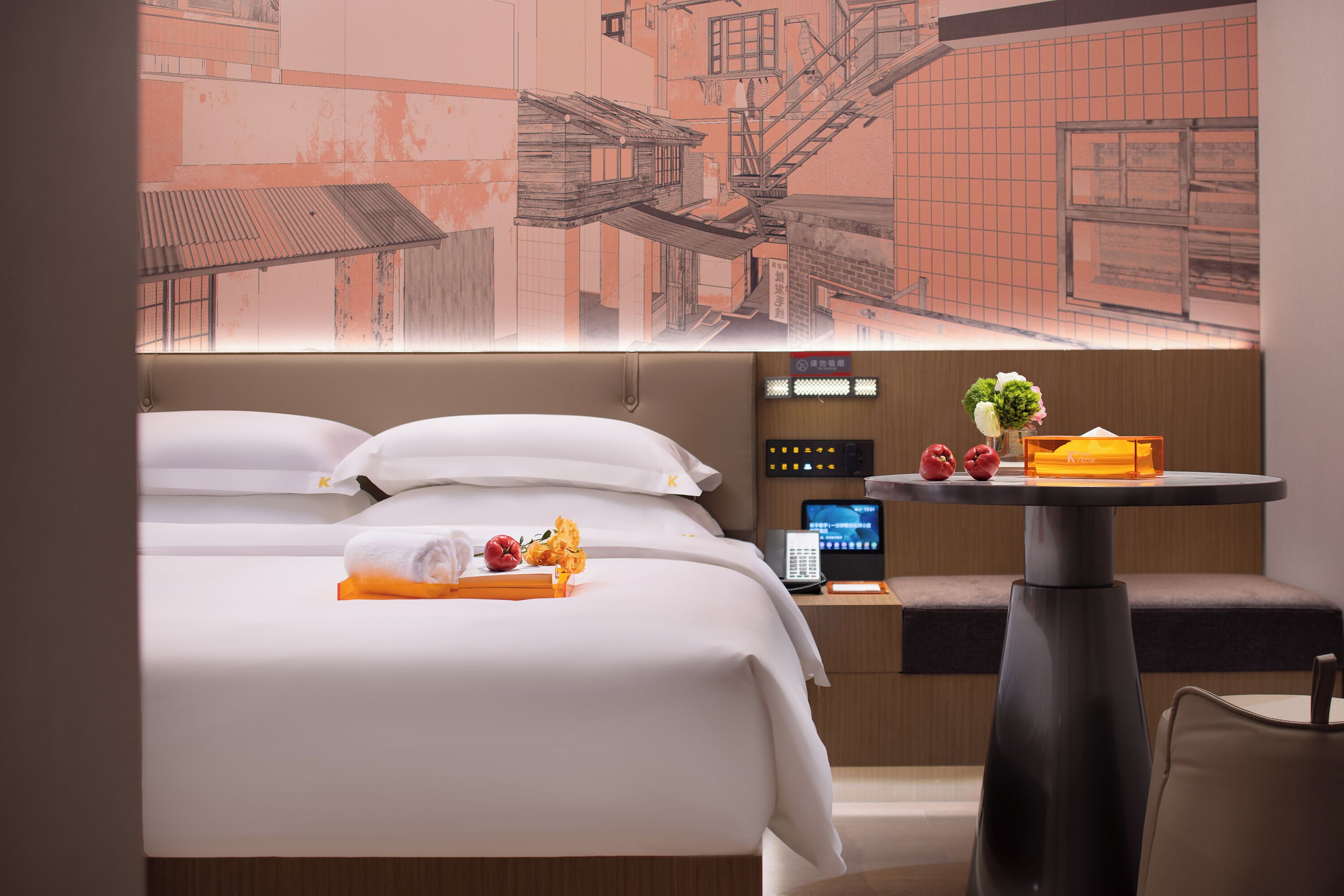 Et hotelværelse med en seng, et lille bord med en vase blomster og et digitalt kontrolpanel.