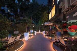 Un'area patio all'aperto con posti a sedere e fioriere, circondata da alberi ed edifici.