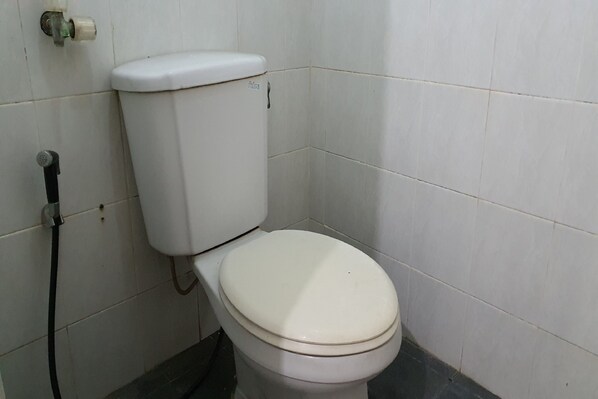 A white toilet with a tank and seat, a visible water pipe, and a wall-mounted flush handle.