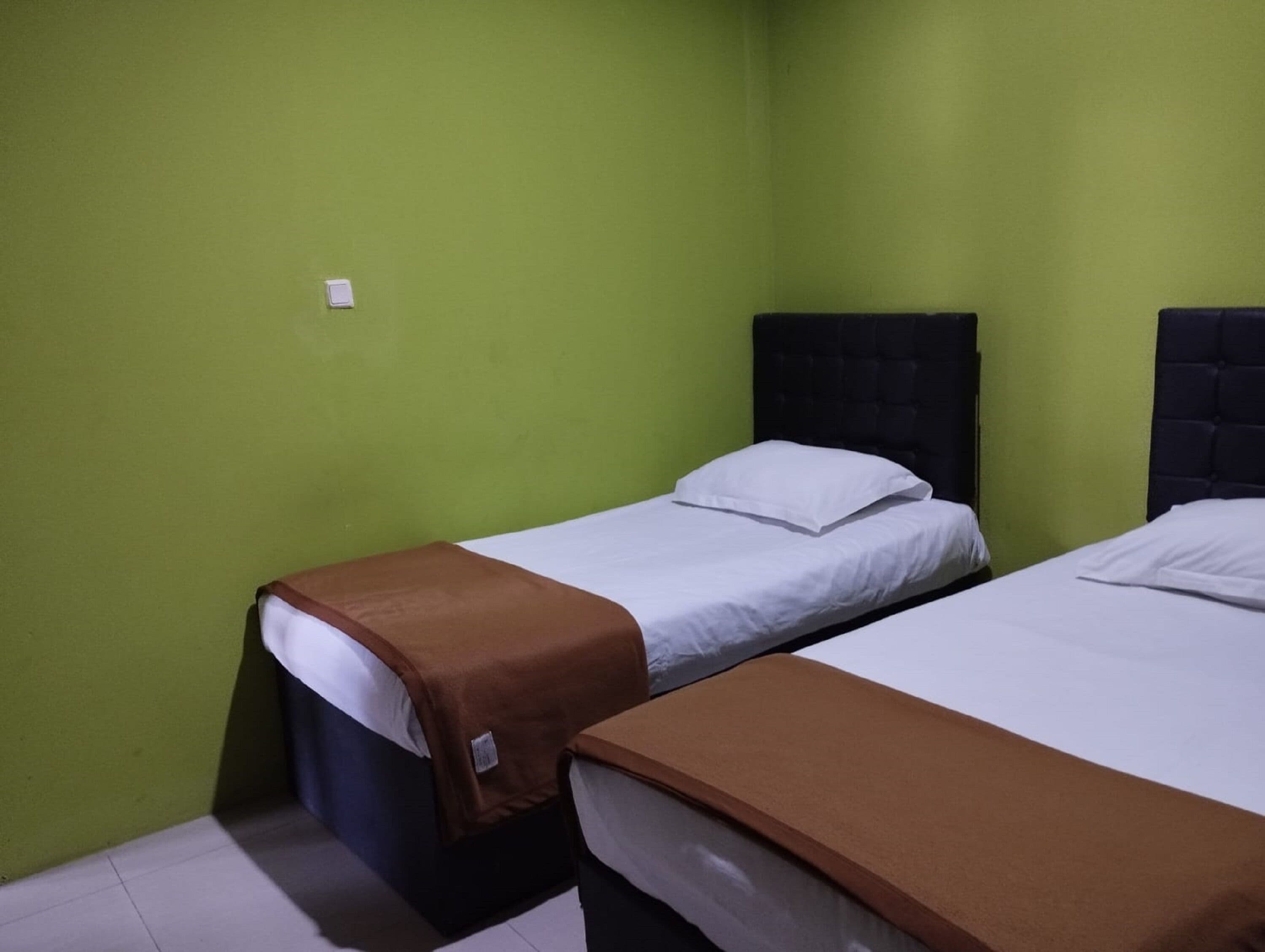 A small, single-room hotel room with two beds, green walls, and a simple, functional design.
